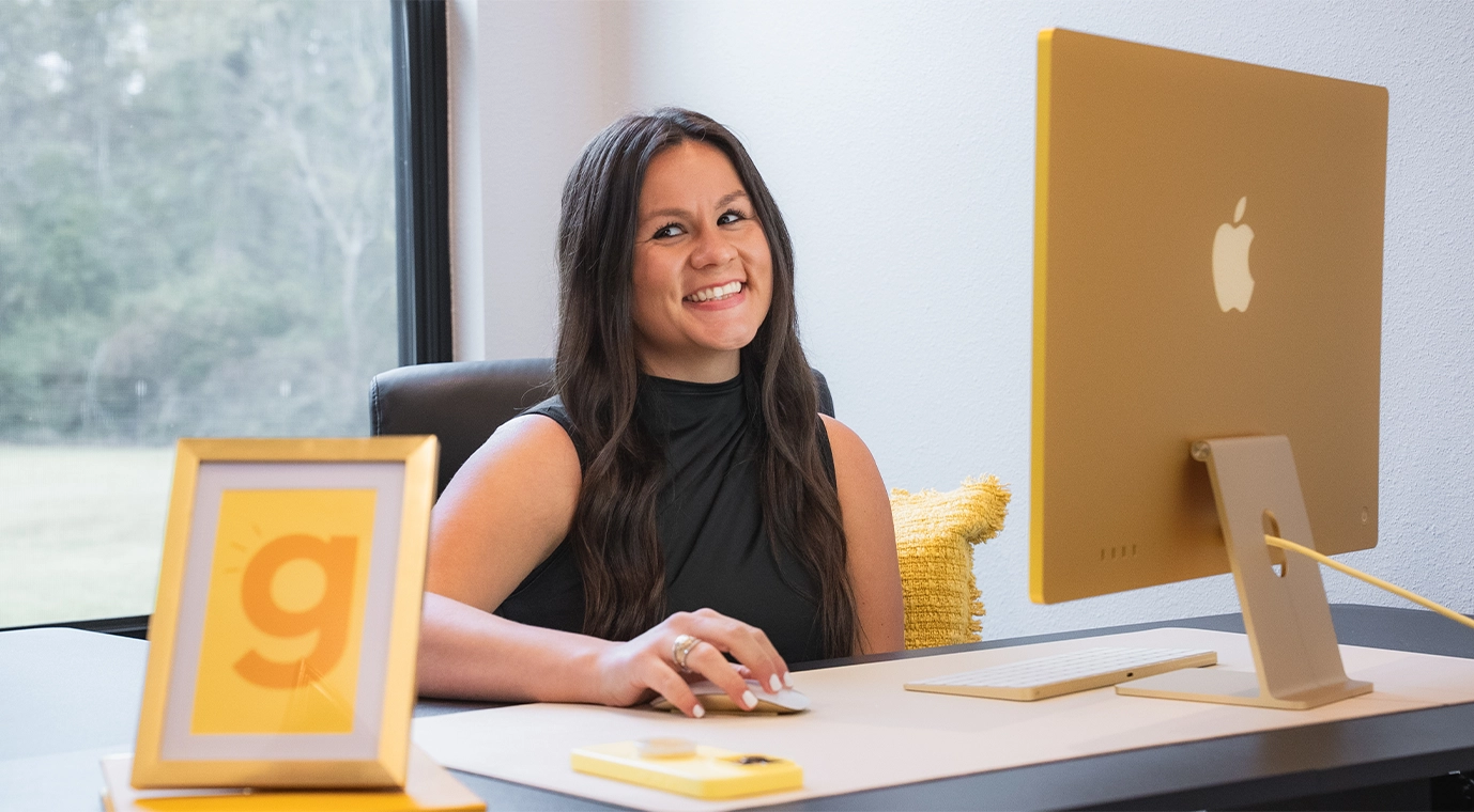 Founder working at a modern desk setup, smiling while using a desktop computer in a bright office workspace.